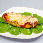 Chicken Parmesan on a bed of spinach with a sprinkle of fresh parmesan cheese on top on a white plate