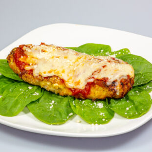 Chicken Parmesan on a bed of spinach with a sprinkle of fresh parmesan cheese on top on a white plate