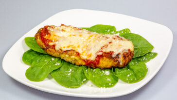 Chicken Parmesan on a bed of spinach with a sprinkle of fresh parmesan cheese on top on a white plate
