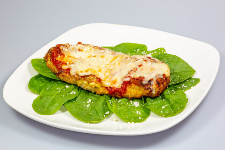 Chicken Parmesan on a bed of spinach with a sprinkle of fresh parmesan cheese on top on a white plate