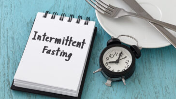 Intermittent fasting word on notepad with clock, fork and knife on white plate, intermittent fasting and weight loss  concept