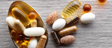 Close-up tablespoon filled with various dietary supplements, tablets and vitamins on a gray fabric background
