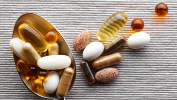 Close-up tablespoon filled with various dietary supplements, tablets and vitamins on a gray fabric background