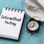 Intermittent fasting word on notepad with clock, fork and knife on white plate, intermittent fasting and weight loss  concept