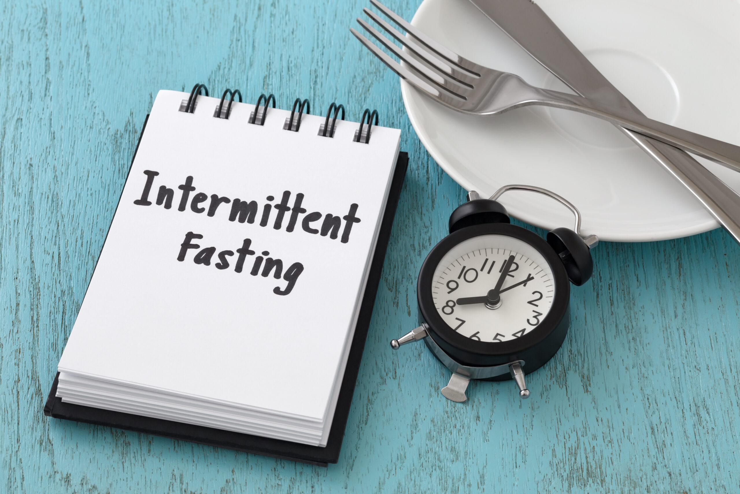 Intermittent fasting word on notepad with clock, fork and knife on white plate, intermittent fasting and weight loss  concept
