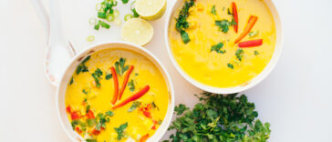 Two bowls of fresh coconut curry soup with cut green parsley, slices of lime, spoons, isolated over white background. Curry bowl for dinner. Vegetarian food concept