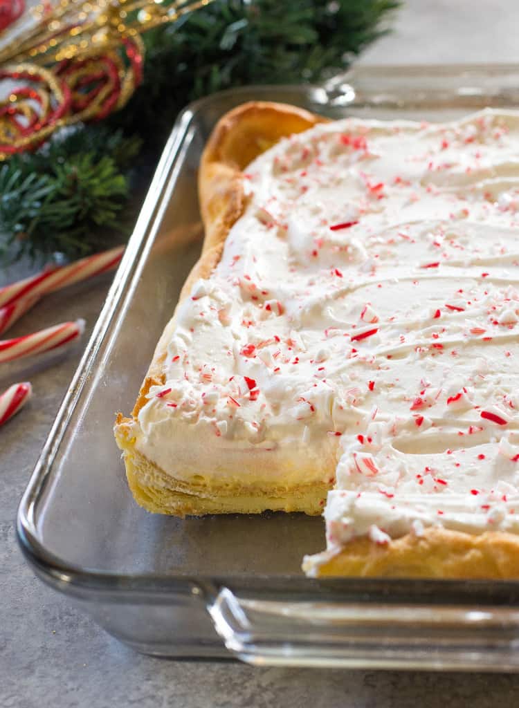 This Eggnog Éclair Cake is a unique holiday dessert with a cream puff crust, creamy eggnog layer, and topped with fresh cream and crushed peppermint candies.