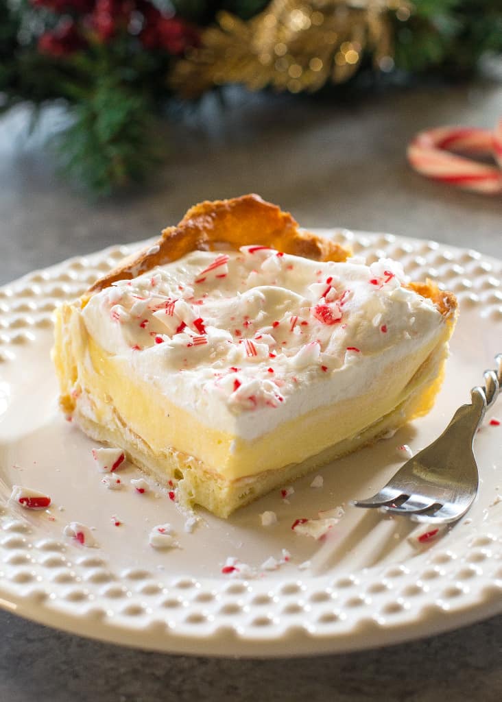 This Eggnog Éclair Cake is a unique holiday dessert with a cream puff crust, creamy eggnog layer, and topped with fresh cream and crushed peppermint candies.