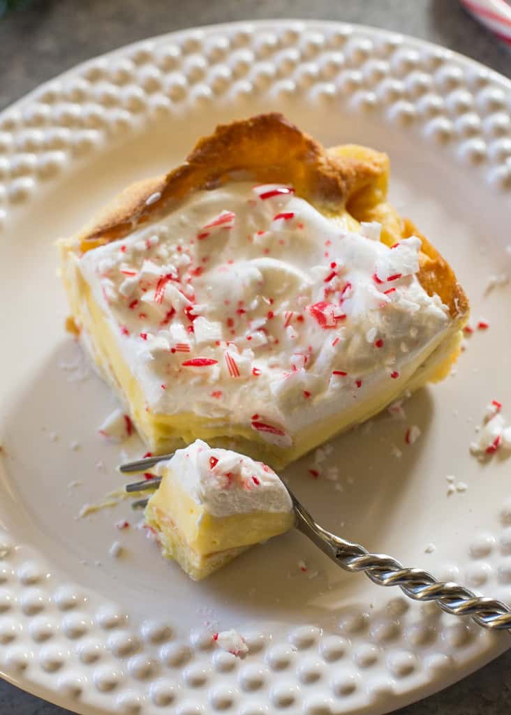 This Eggnog Éclair Cake is a unique holiday dessert with a cream puff crust, creamy eggnog layer, and topped with fresh cream and crushed peppermint candies.