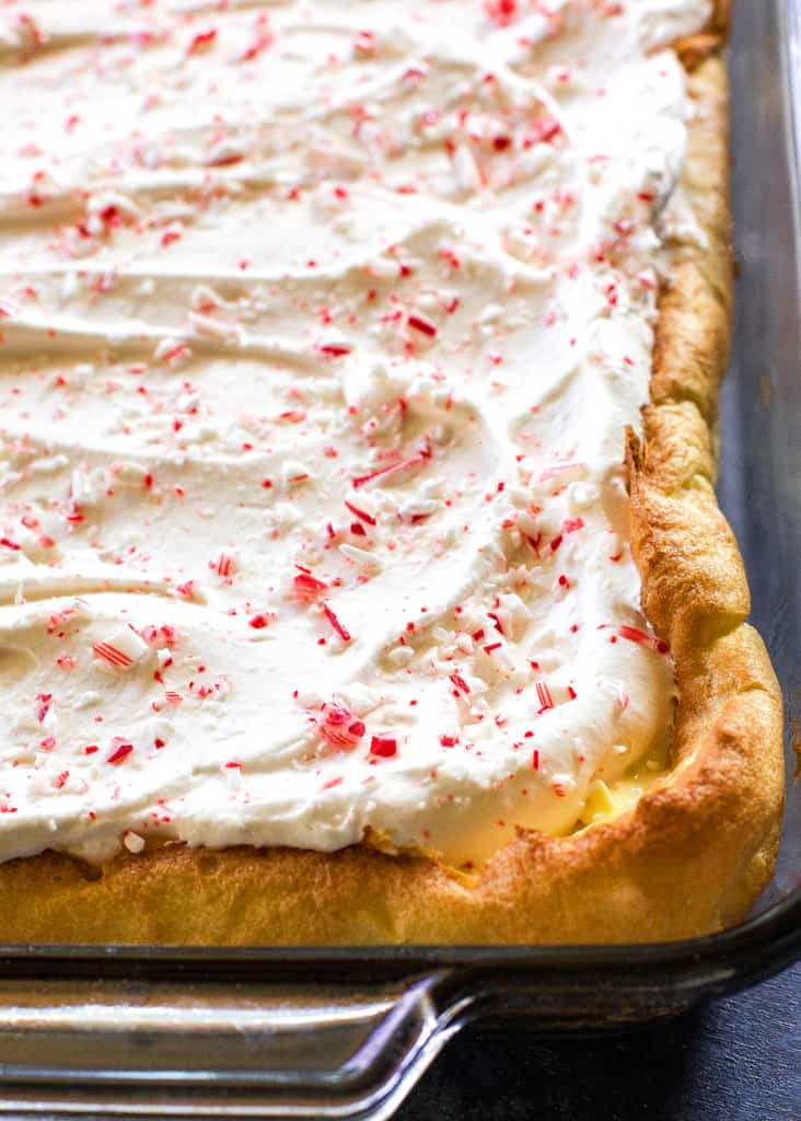 This Eggnog Éclair Cake is a unique holiday dessert with a cream puff crust, creamy eggnog layer, and topped with fresh cream and crushed peppermint candies.